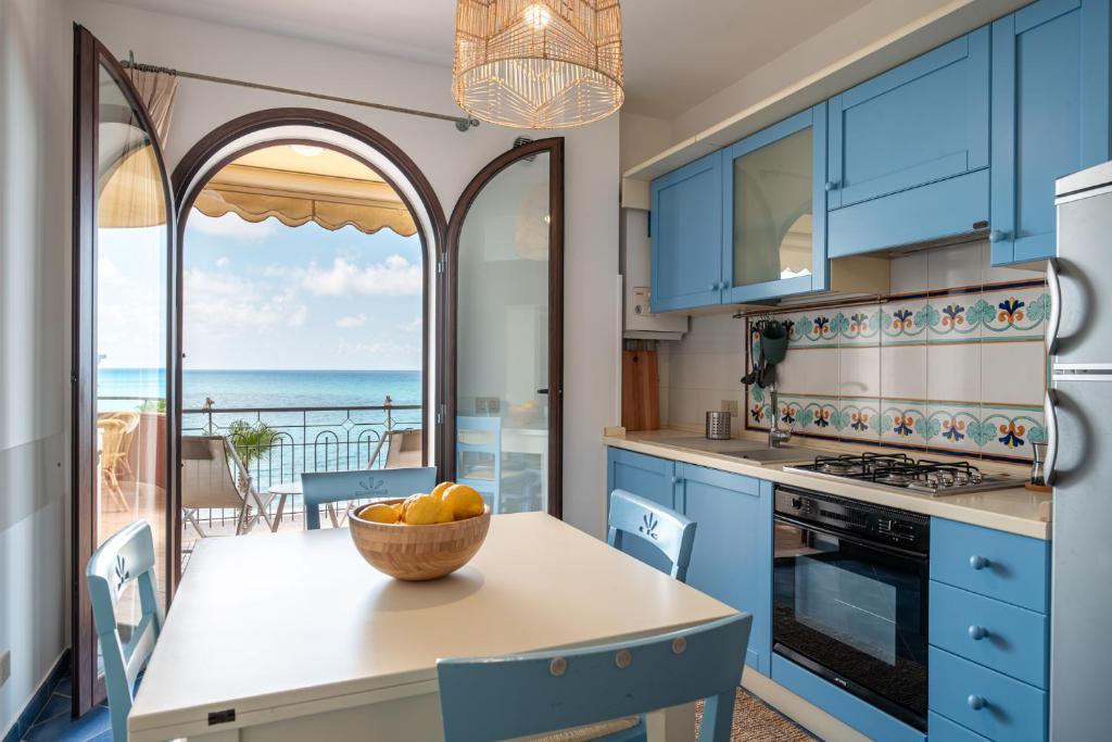 una cocina con armarios azules y una mesa con un bol de fruta en Residence L'Arcipelago Appartamenti Fronte Mare con Ampio Balcone, en Capo dʼOrlando