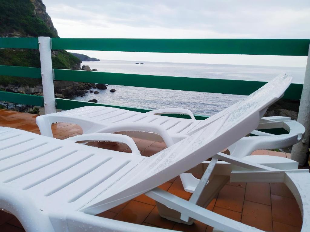 twee witte stoelen op een balkon met uitzicht op de oceaan bij PARAISO ESTAÑO, Terraza PRIMERA LINEA DE PLAYA in Gijón