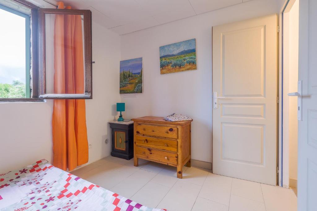 a bedroom with a bed and a wooden dresser and a door at Calenzana Trè - Appt avec piscine partagée in Calvi