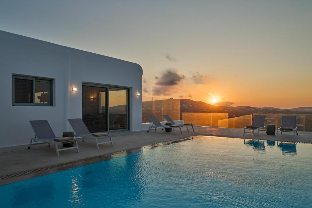 a pool with chairs and the sunset in the background at Villa j-view in Psarou