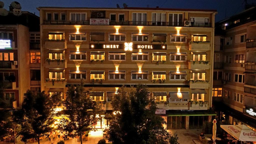 a tall building with lights on it at night at Emery Hotel in Prishtinë