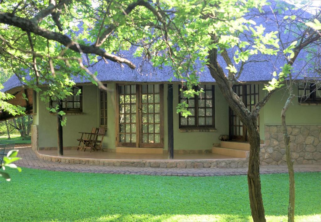 a green house with a tree in front of it at Family Lodge in Natural African bush - 2113 in Bulawayo