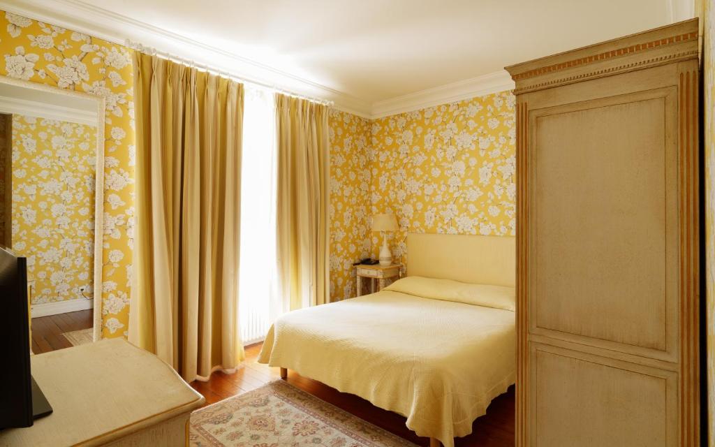 1 dormitorio con cama con papel pintado de color amarillo y ventana en Hôtel de Margaux, en Margaux
