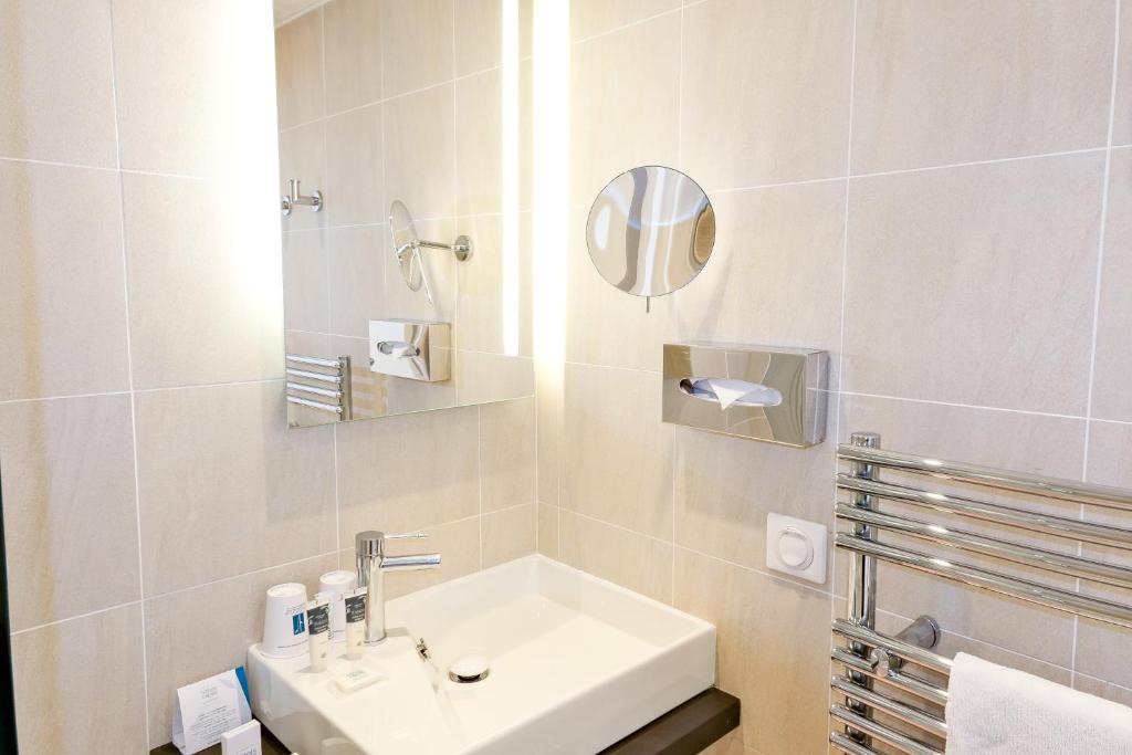 a white bathroom with a sink and a mirror at Thalazur Ouistreham - Hôtel & Spa in Ouistreham