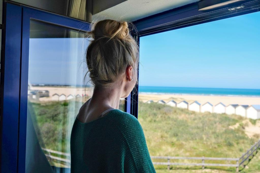 a woman looking out a window at the beach at Thalazur Ouistreham - Hôtel & Spa in Ouistreham