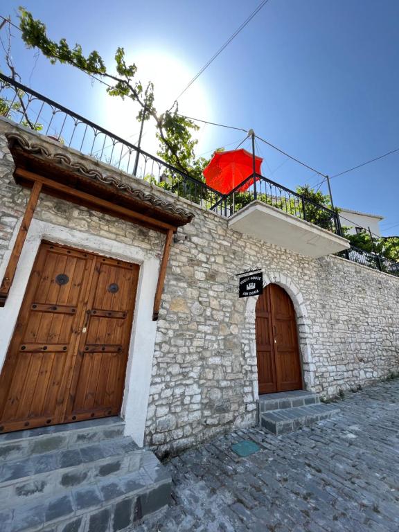 Casa con 2 puertas de madera y sombrilla roja en Guest House Adi Doga, en Berat