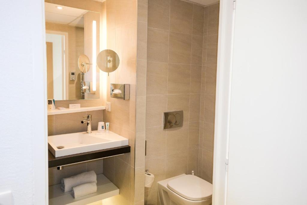 a bathroom with a sink and a toilet and a mirror at Thalazur Ouistreham - Hôtel & Spa in Ouistreham