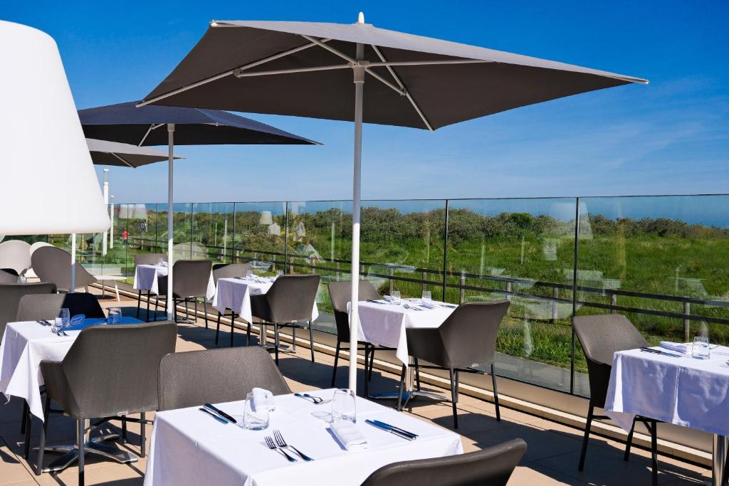 a restaurant with tables and umbrellas on a balcony at Thalazur Ouistreham - Hôtel & Spa in Ouistreham