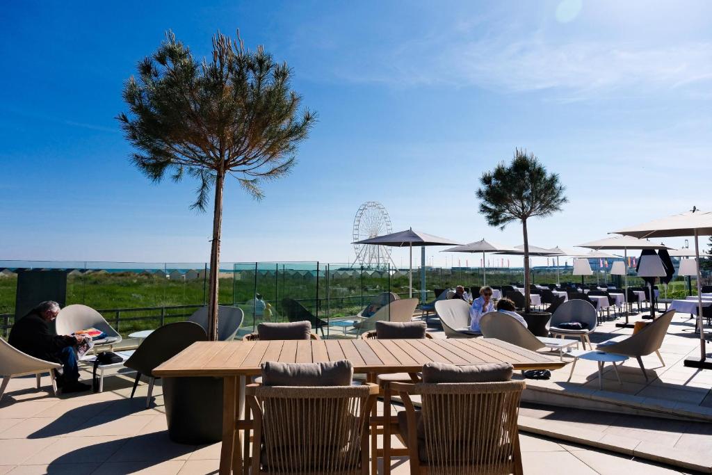 un patio con mesas, sillas y un árbol en Thalazur Ouistreham - Hôtel & Spa, en Ouistreham