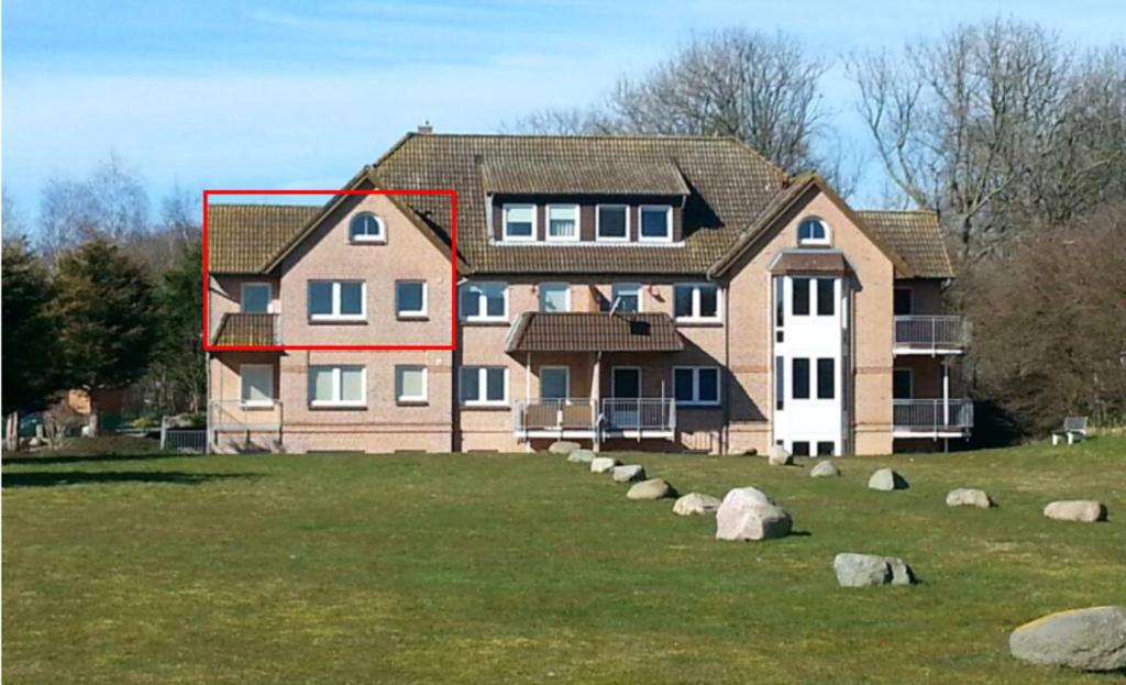 una casa grande en un campo con rocas delante de ella en Fehmarn-OstseeferienSeeblick204, en Fehmarn