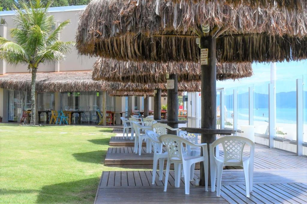 uma fila de cadeiras e mesas brancas debaixo de um guarda-chuva de palha em Pousada Holiday em Florianópolis