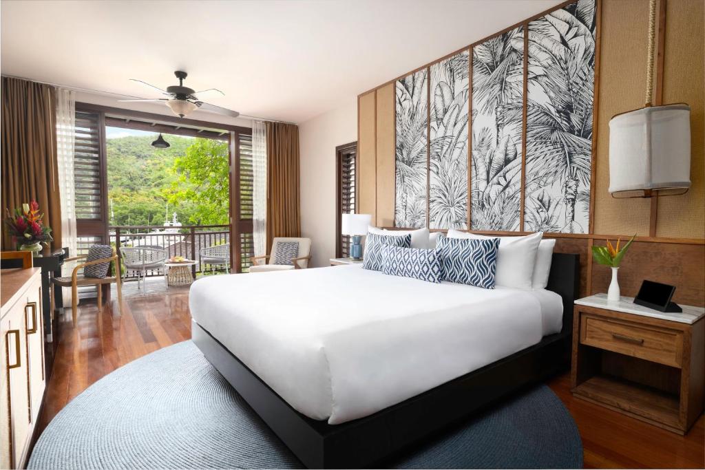 Bedroom with king bed, palm-patterned headboard, balcony overlooking tropical greenery.