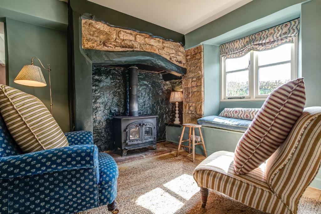 a living room with two chairs and a wood stove at Church End Cottage in Swerford