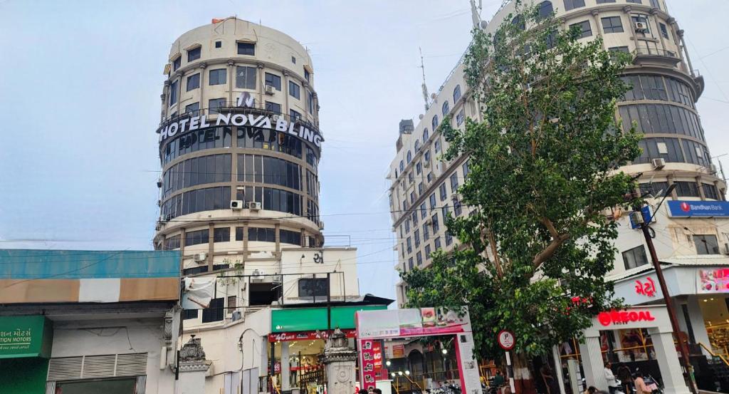 two tall buildings on a city street with a tree at Hotel Nova Bling in Rajkot