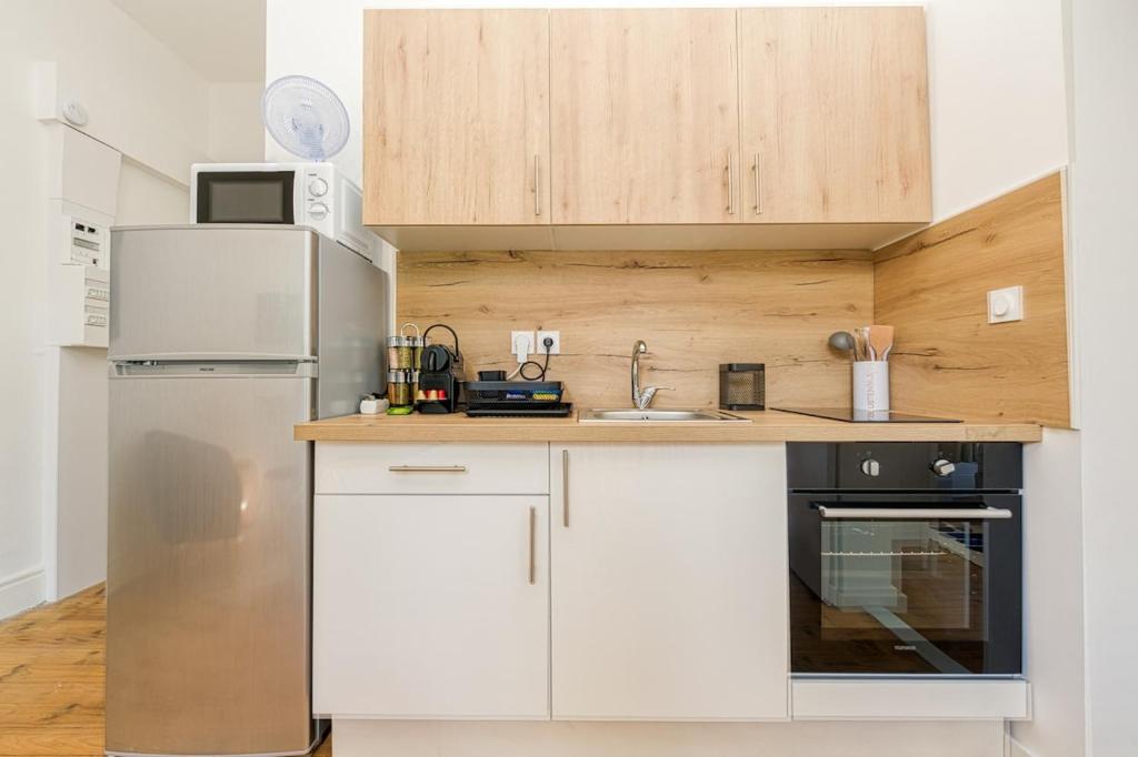 a kitchen with white cabinets and a stainless steel refrigerator at 2 pièces tout confort, déco moderne, wifi fibre in Grenoble