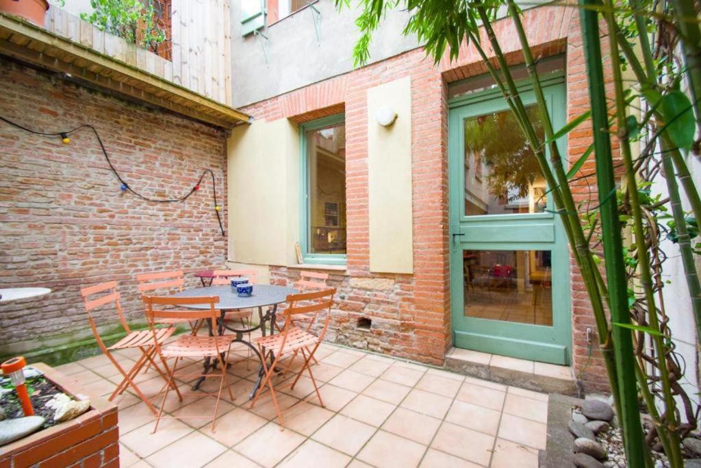 un patio avec une table et des chaises et un mur de briques dans l'établissement La maison du Merle: le charme en centre-ville, à Toulouse