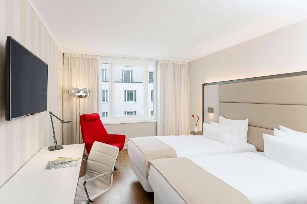 a hotel room with two beds and a red chair at NH Collection Berlin Mitte am Checkpoint Charlie in Berlin