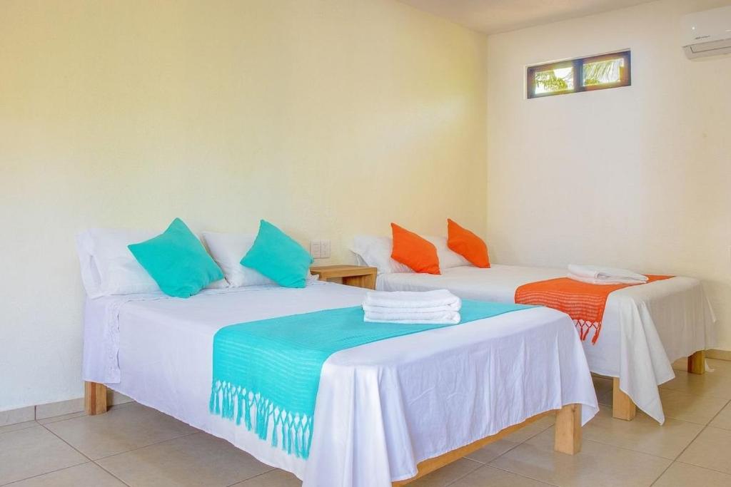 two beds in a room with blue and orange pillows at Casa Yoo Bigu Mazunte in Mazunte