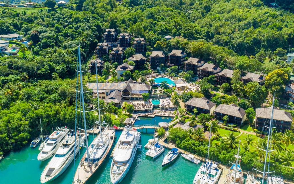 Aerial view of beachfront resort with pools, sailing boats, and tropical forest surrounding the property.