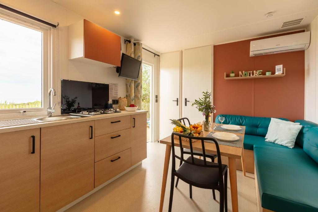cocina y sala de estar con sofá azul y mesa en Le Cycas, mobil-home neuf avec sa vue dégagée sur les vignes et la mer, en Hyères