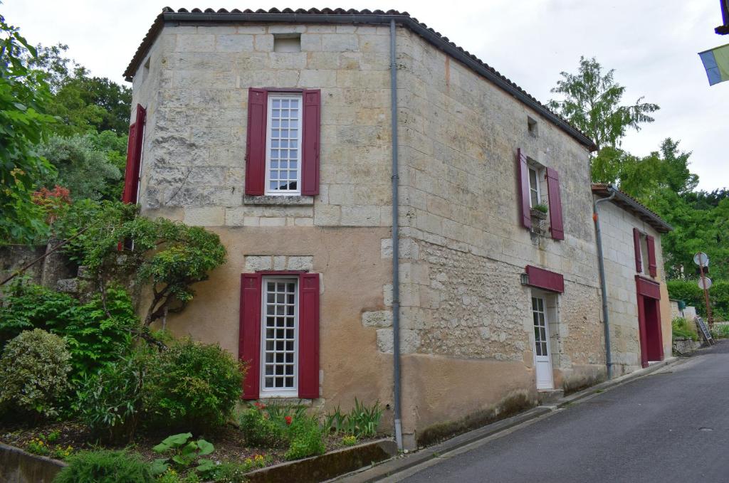 een oud stenen gebouw met rode luiken op een straat bij La Maison du Tourniquet in Aubeterre-sur-Dronne