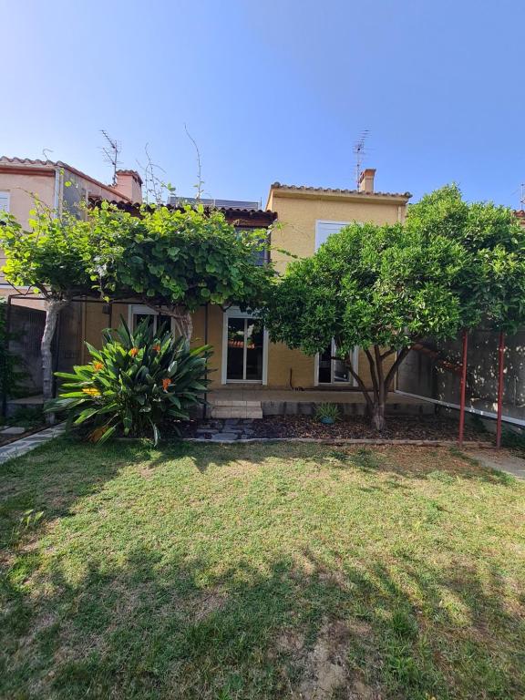 une maison jaune avec des arbres devant une cour dans l'établissement La maison ensoleillée, à Rivesaltes