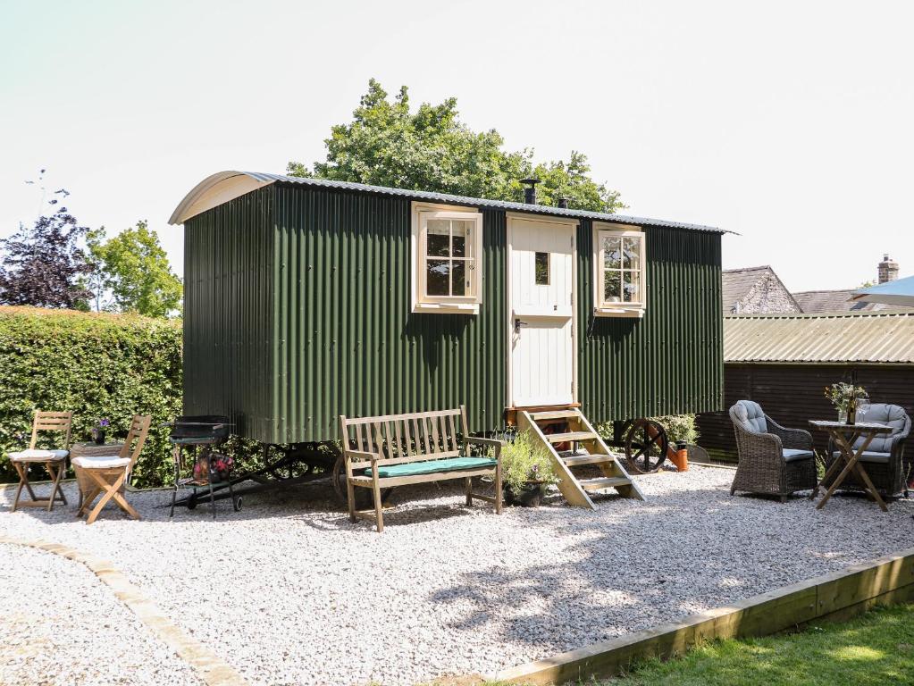 a green tiny house with a bench and chairs at Shepherd's Hut in Castleton