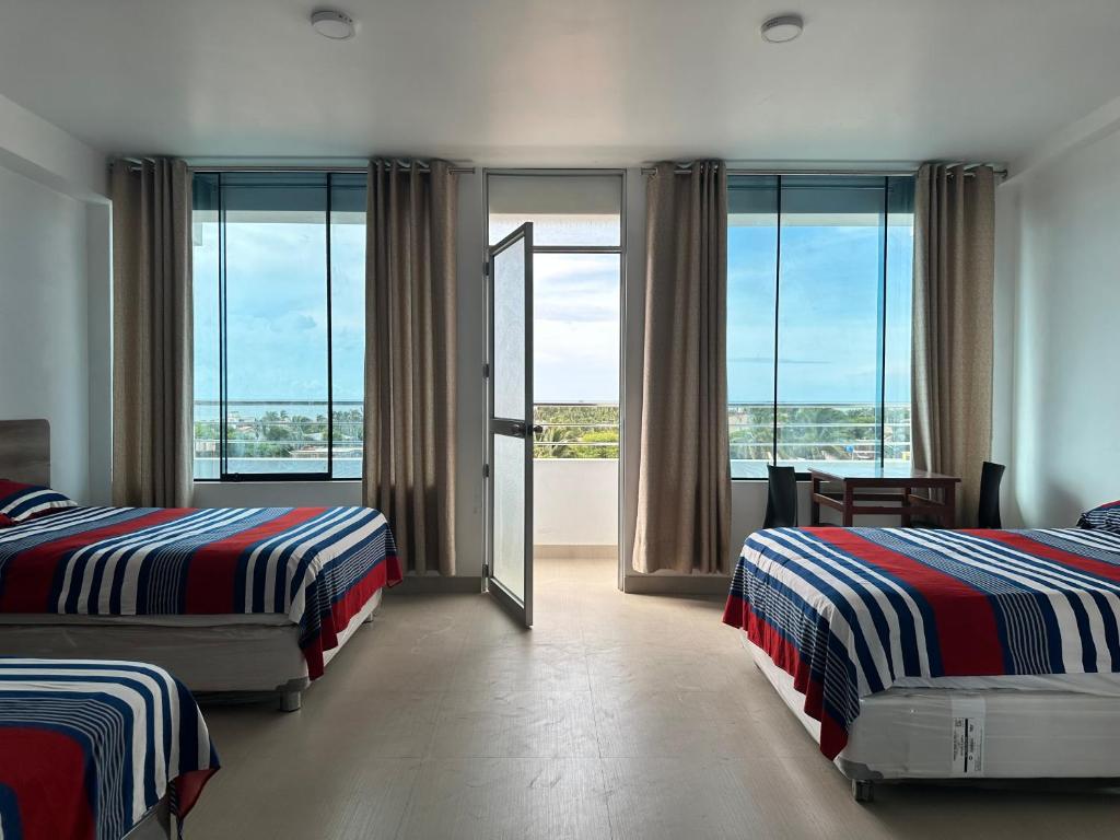 a bedroom with two beds and a balcony with windows at Camber Inn Hotel in Máncora