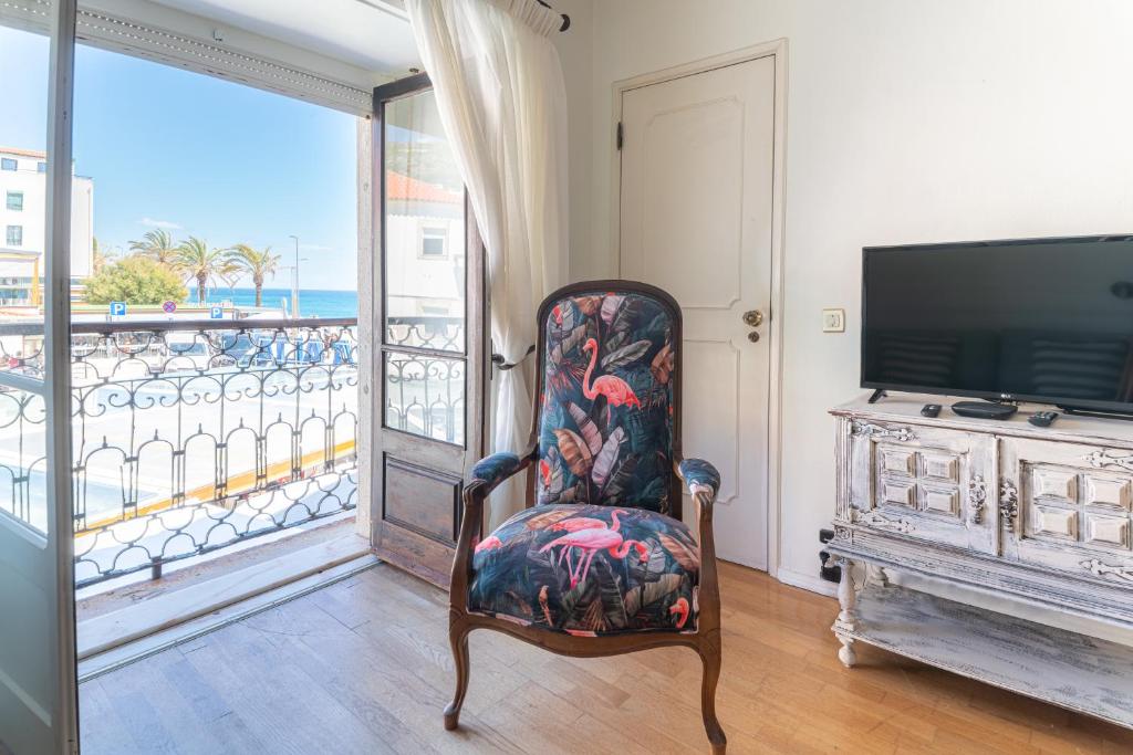 a room with a chair and a television and a balcony at Apartamento Fortaleza in Sesimbra