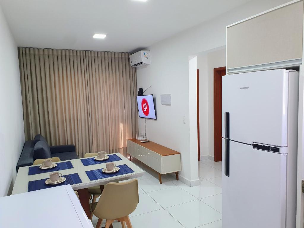 ein Wohnzimmer mit einem Tisch und einem Kühlschrank in der Unterkunft Apt próx. Shopping Pantanal/Centro Político in Cuiabá