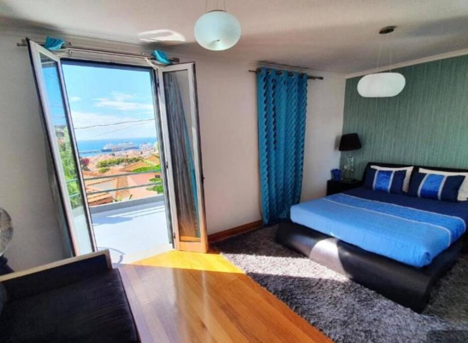 sypialnia z niebieskim łóżkiem i dużym oknem w obiekcie O farol do funchal w Funchal