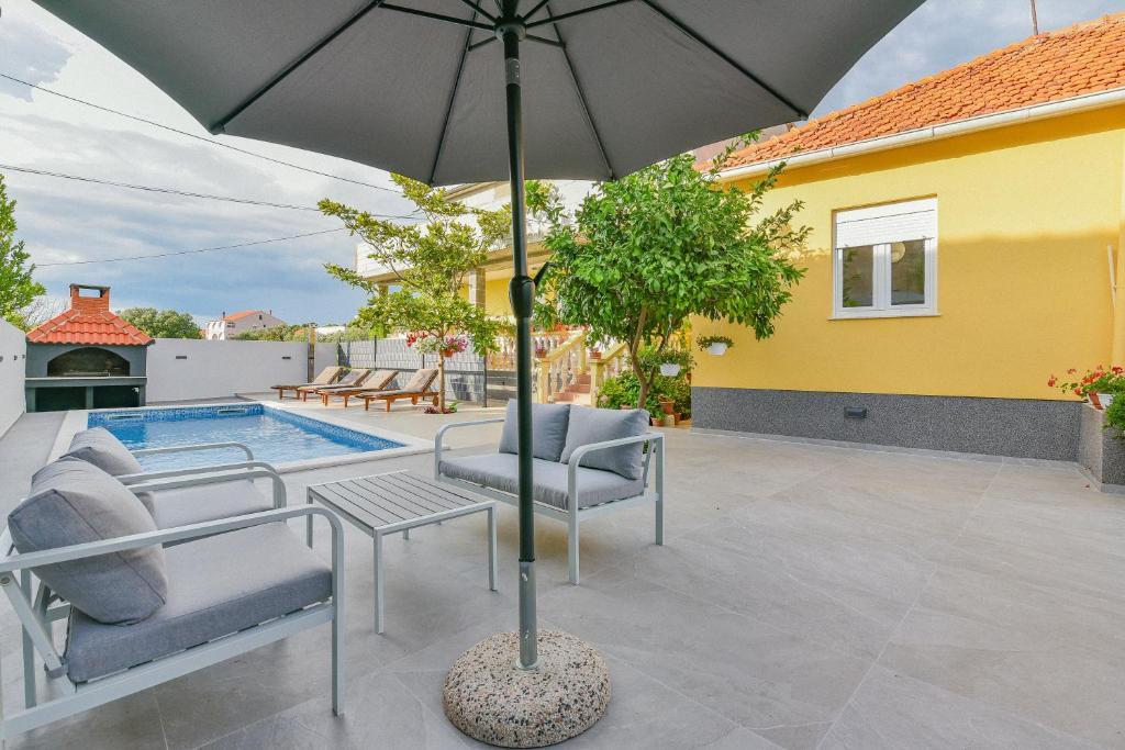 a patio with an umbrella and chairs and a pool at Holiday homEna with a heated pool in Bibinje