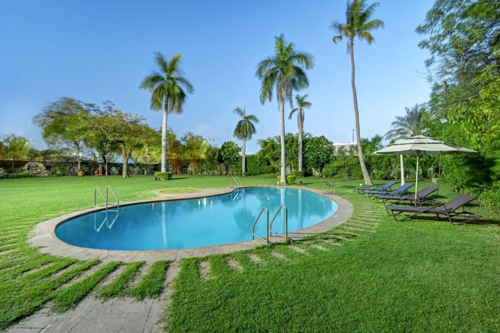 uma piscina com cadeiras e guarda-sóis e palmeiras em The Cama - A Sabarmati Riverfront Hotel em Ahmedabad