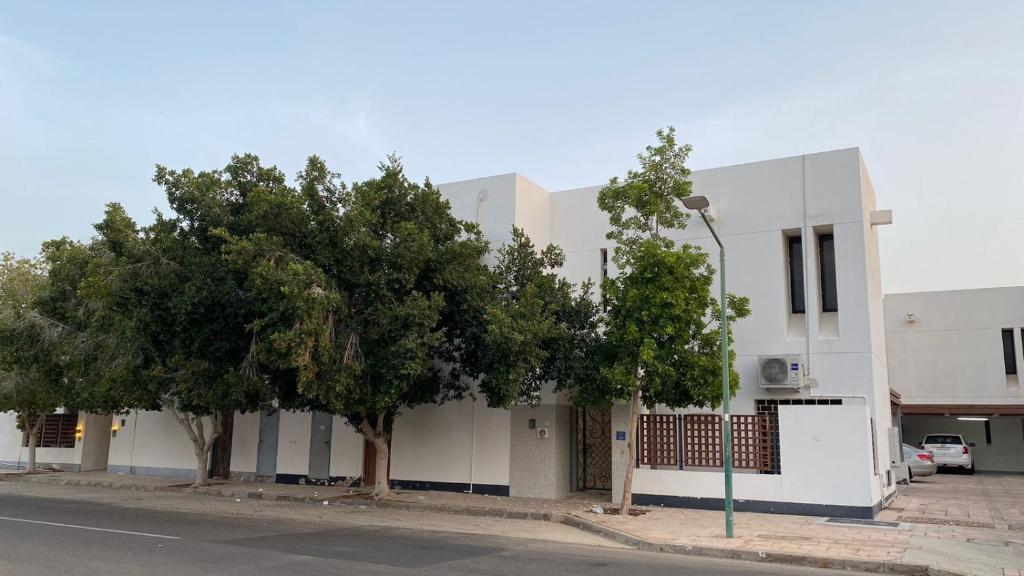 biały budynek z drzewami przed nim w obiekcie فيلا رضوى الخير w mieście Madīnat Yanbu‘ aş Şinā‘īyah