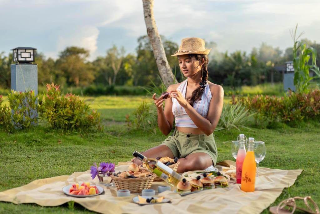 Una mujer con sombrero sentada en una manta de picnic en Elephyard Retreat, en Mahiyangana