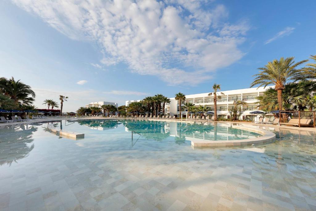 a large swimming pool with palm trees and a building at Grand Palladium Palace Ibiza Resort & Spa- All Inclusive in Playa d'en Bossa