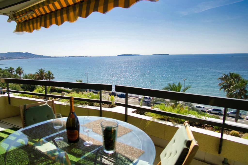 una mesa con una botella de vino en el balcón con vistas al océano en Ref EGEE - Palmes d'Or Properties en Cannes