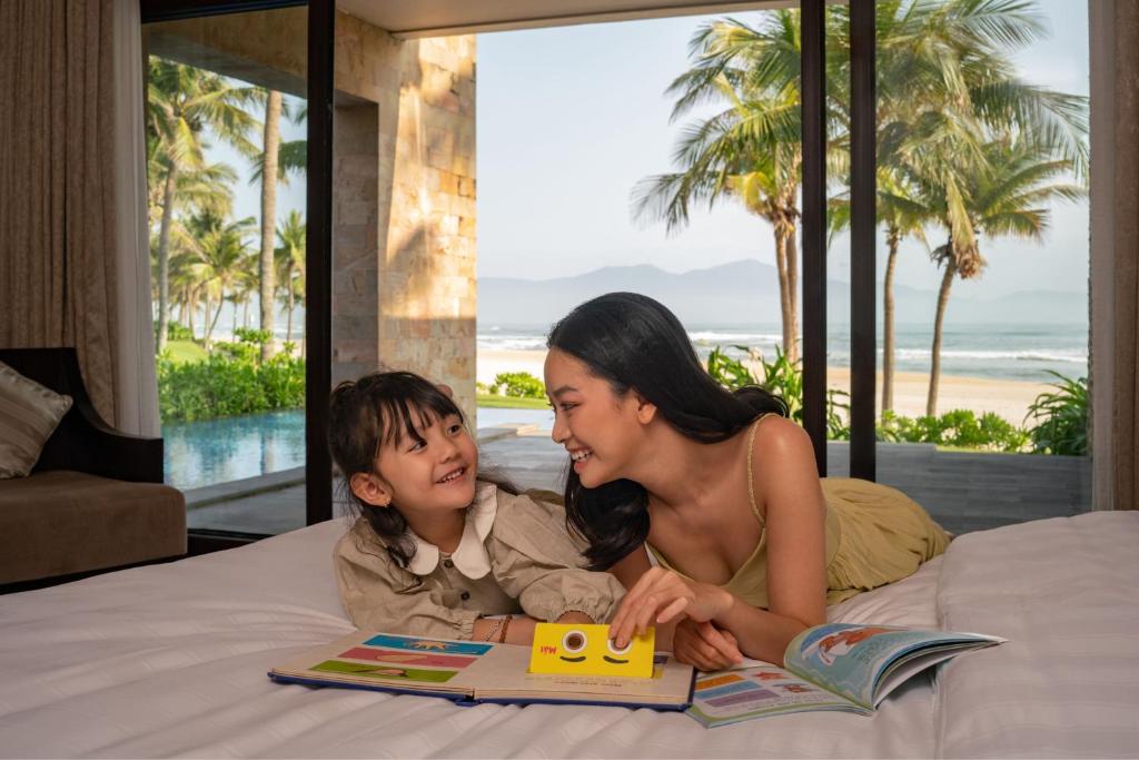 A family uses a bed beside glass doors overlooking the coast.
