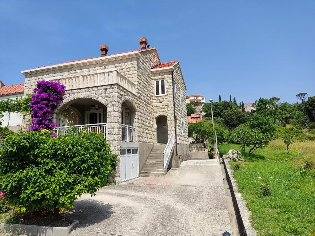 una gran casa de piedra con una puerta y flores púrpuras en Guest House Franica & Pero Lobrovic, en Slano