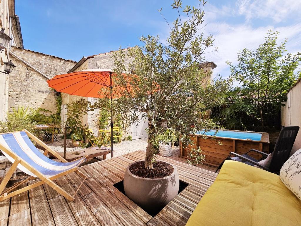 eine Terrasse mit einem Baum, einem Stuhl und einem Sonnenschirm in der Unterkunft Sublime maison charentaise in Jarnac