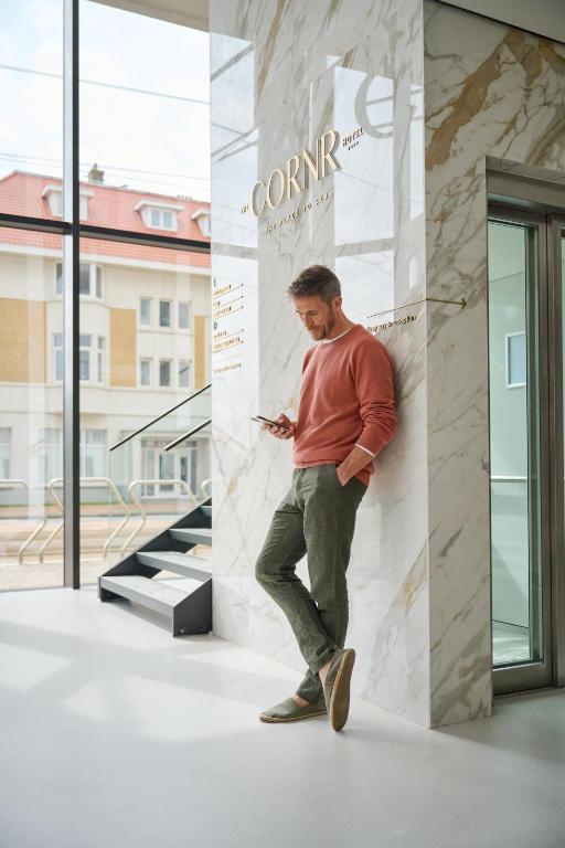 Ein Mann, der sich an die Wand lehnt und sein Handy ansieht. in der Unterkunft The CORNR Hotel in Nieuwpoort