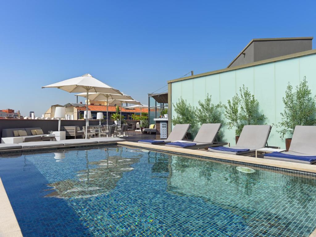 a pool with lounge chairs and an umbrella on a building at H10 Casanova in Barcelona