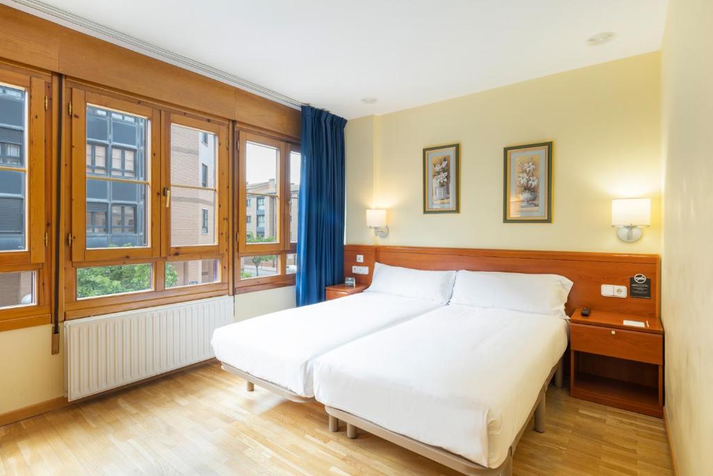 a bedroom with a large white bed and windows at Hostal Alda Río Duero in Soria