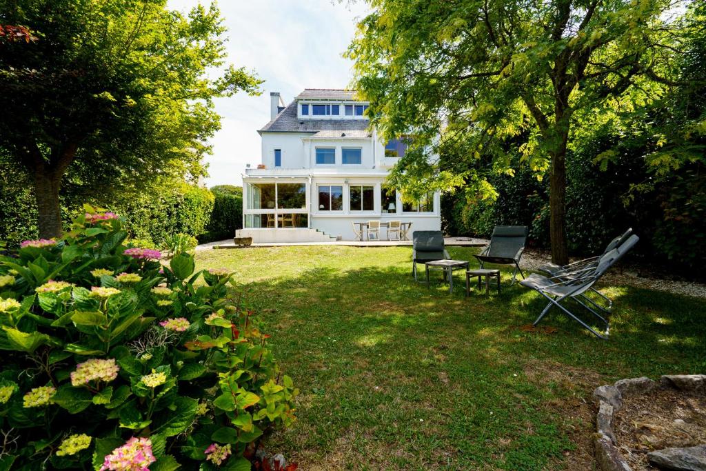 une grande maison blanche avec 2 chaises de jardin et des fleurs dans l'établissement Le Huic - Maison pour 9 avec jardin proche plage, à Bénodet