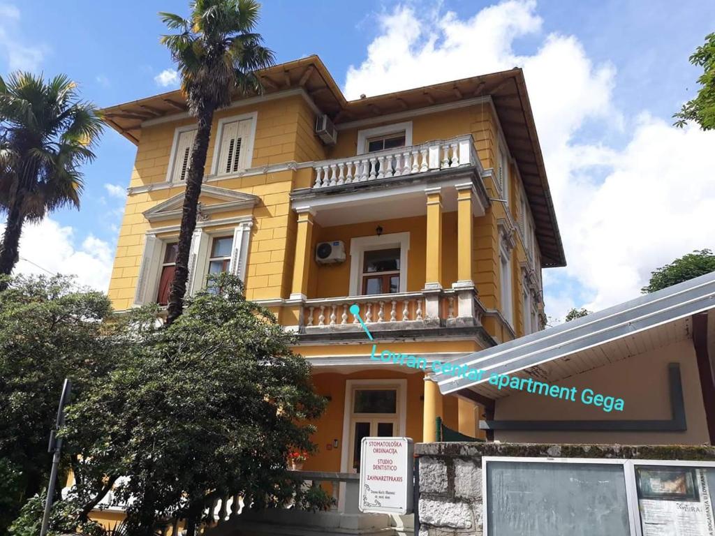 a yellow building with palm trees in front of it at Lovran centar, apartman Gega in Lovran