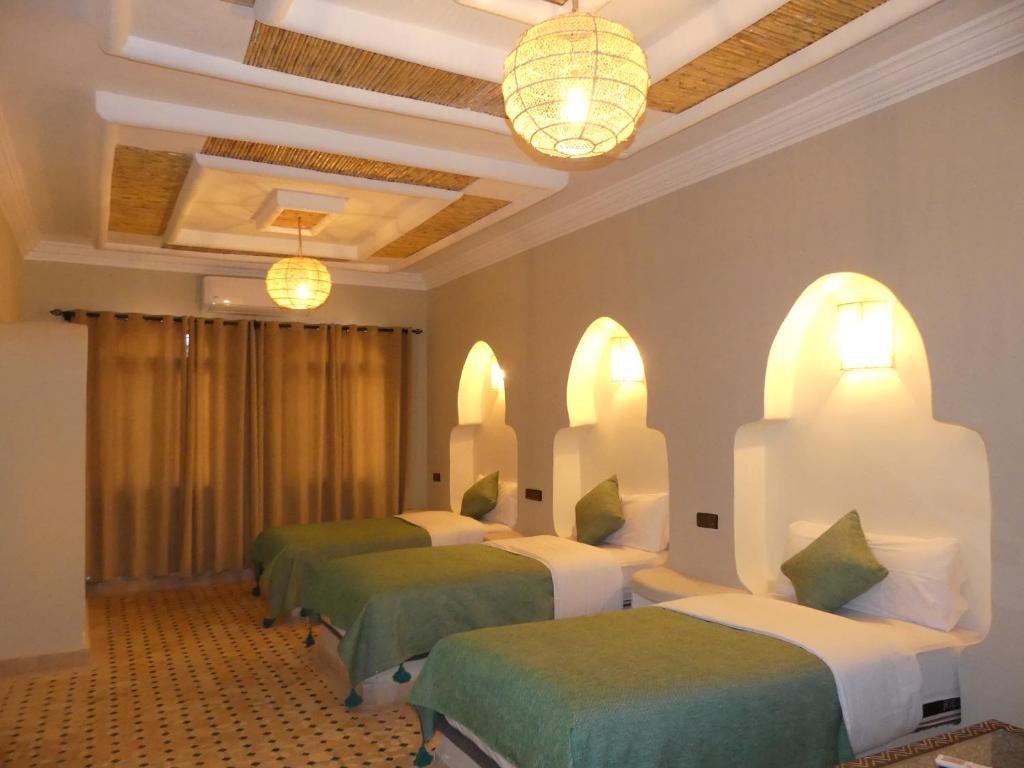 Habitación con 4 camas con sábanas verdes y blancas. en Riad La Luna en Merzouga