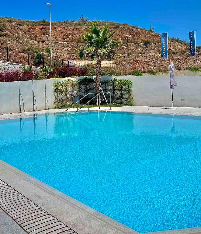 a large blue swimming pool with a palm tree at Rincón Idilia (Málaga). in Rincón de la Victoria