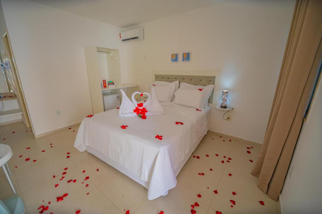 a bedroom with a white bed with red rose petals on the floor at Pousada Polymar in Maragogi