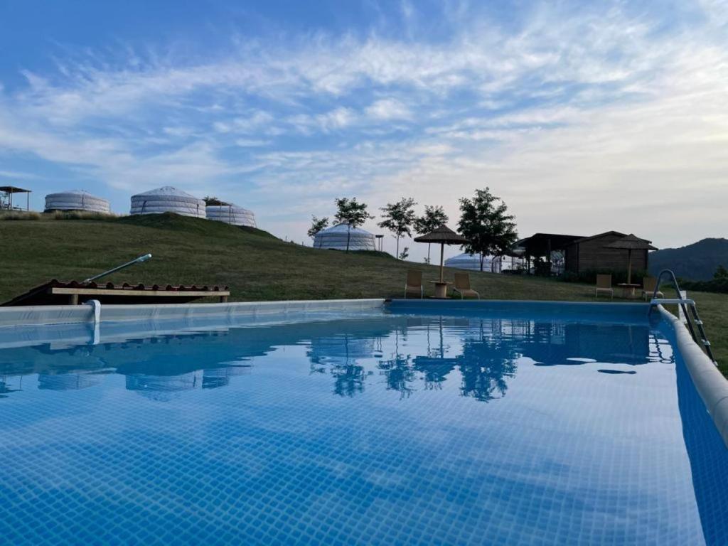 a large blue swimming pool with a hill in the background at Yurte in Langa in Bosia