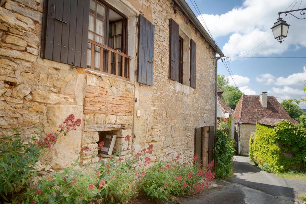 un antiguo edificio de piedra con una ventana y flores en La Petite Maison du Périgord, en Tourtoirac